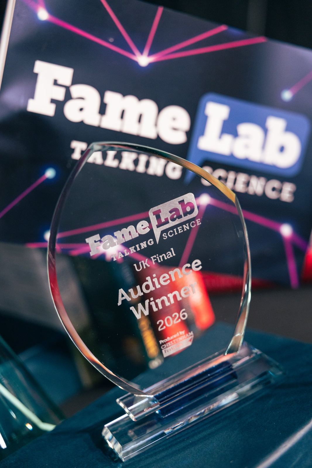 A glass FameLab UK Final Audience Winner 2026 trophy in front of a FameLab Talking Science banner